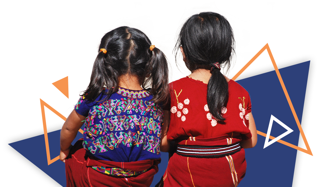 Back view of two young native girls sitting together; they are wearing colorful native apparel
